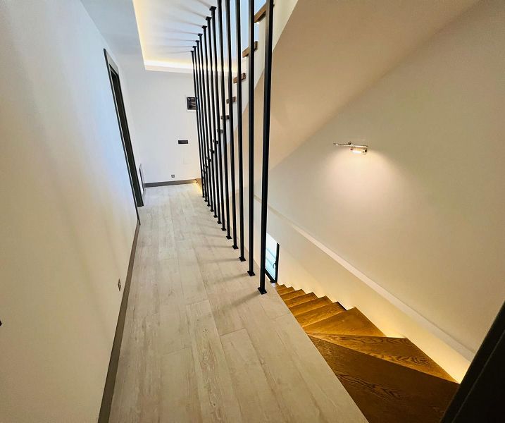 Flur mit hellen Bodenfliesen und Treppe mit Holzstufen und schwarzem Geländer