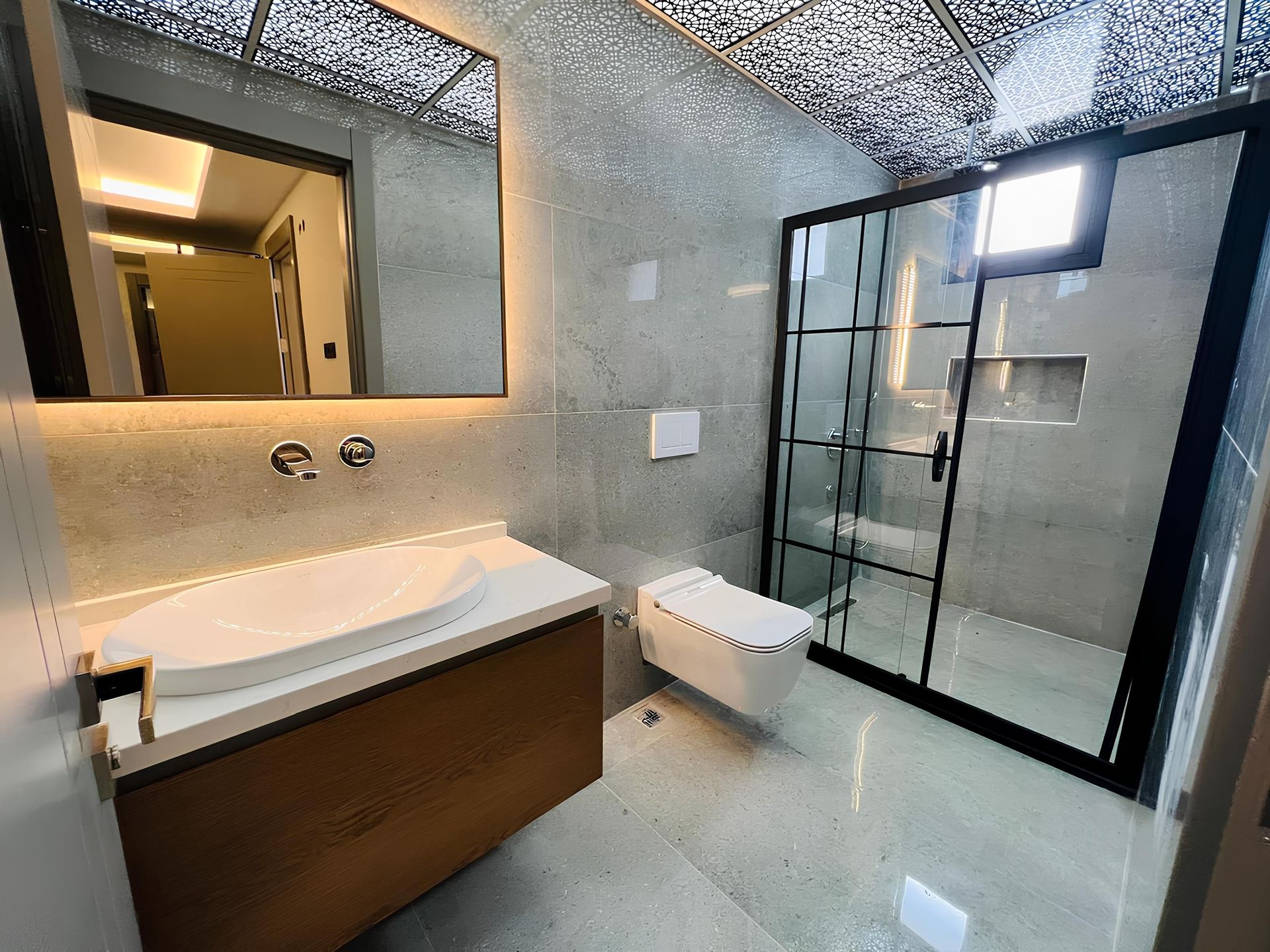 Modernes Badezimmer mit beleuchtetem Spiegel, Waschbecken mit Unterschrank, wandhängendem WC und Duschkabine mit schwarzem Rahmen